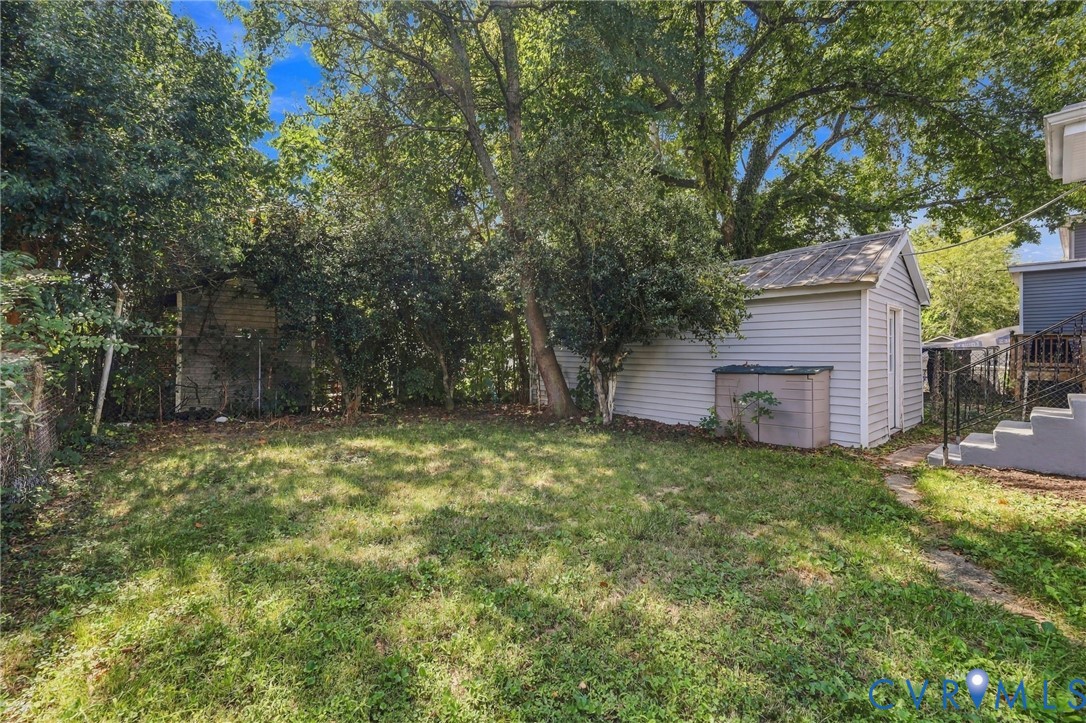 Expansive rear yard featuring a detached storage shed, mature trees, and concrete steps
