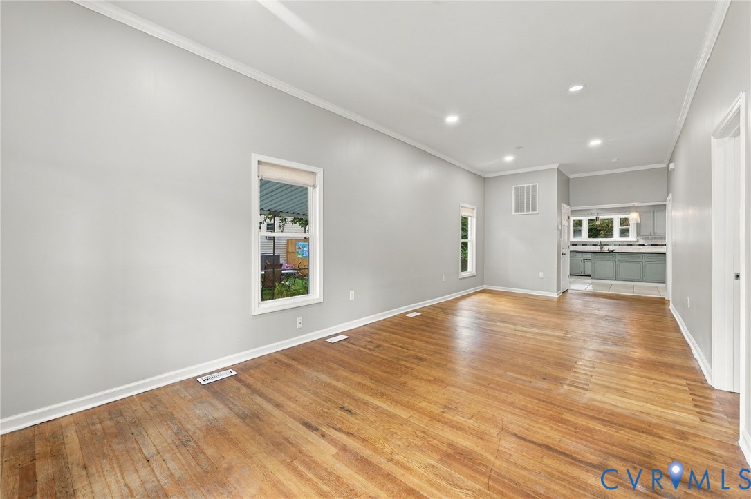 Hardwood flooring, recessed lighting, crown molding, white trim, and a glimpse of the kitchen with painted cabinetry