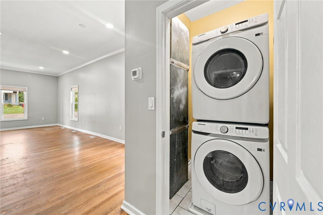 Stacked washer and dryer unit, wood-finish flooring, recessed lighting, and crown molding