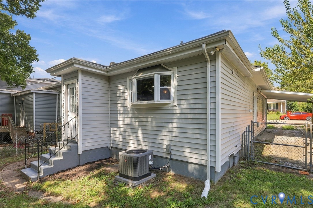 Light gray horizontal siding with white trim, bay window, concrete steps with metal railing, and a fenced area