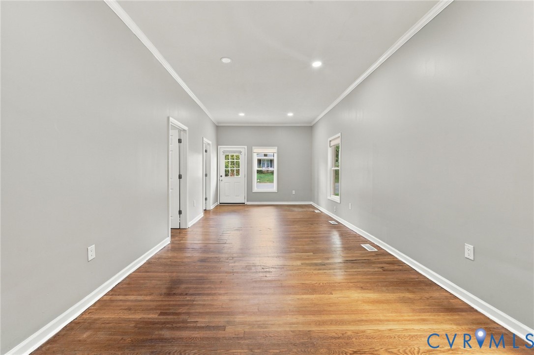 Expansive room with wood-finish flooring, light gray walls, white trim, recessed lighting, and a glass-paneled exterior door