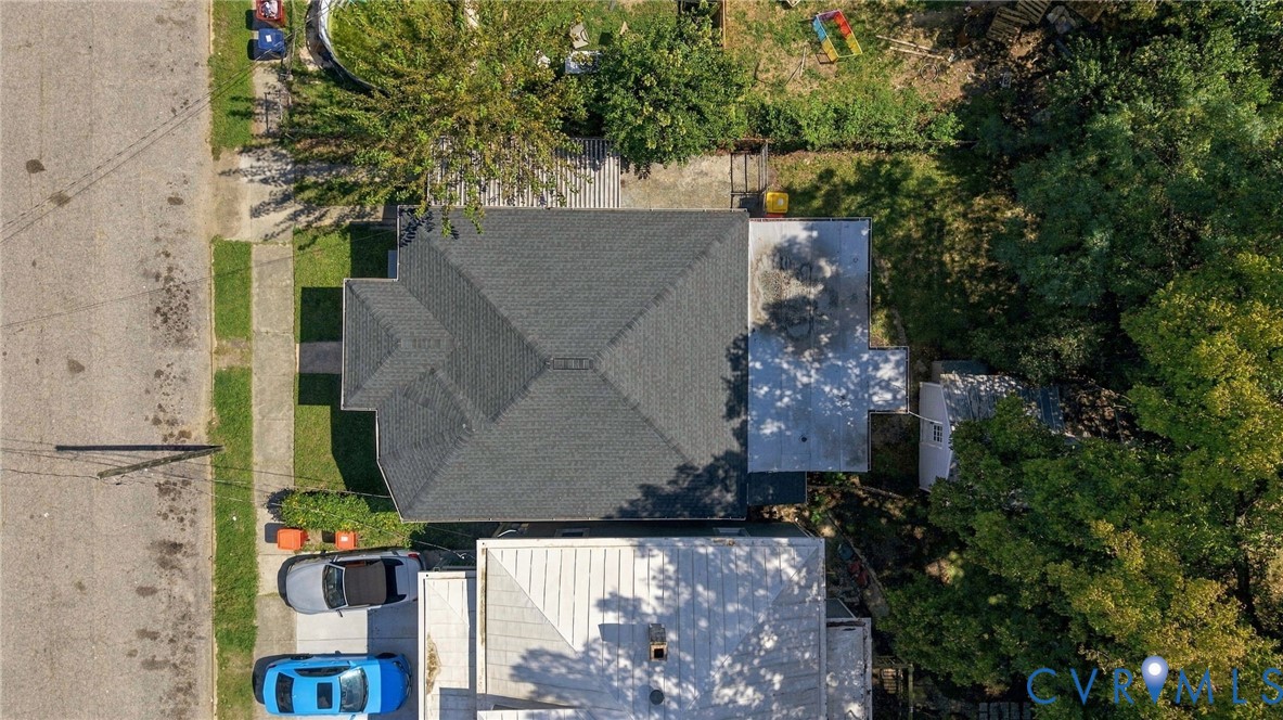 Gable roof with dark shingles, paved driveway, and established trees