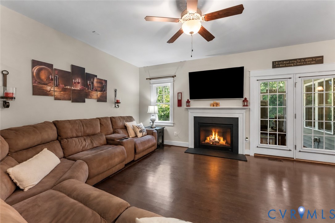 Wood-finish flooring with a ceiling fan, fireplace with white mantel, and double glass-paneled doors