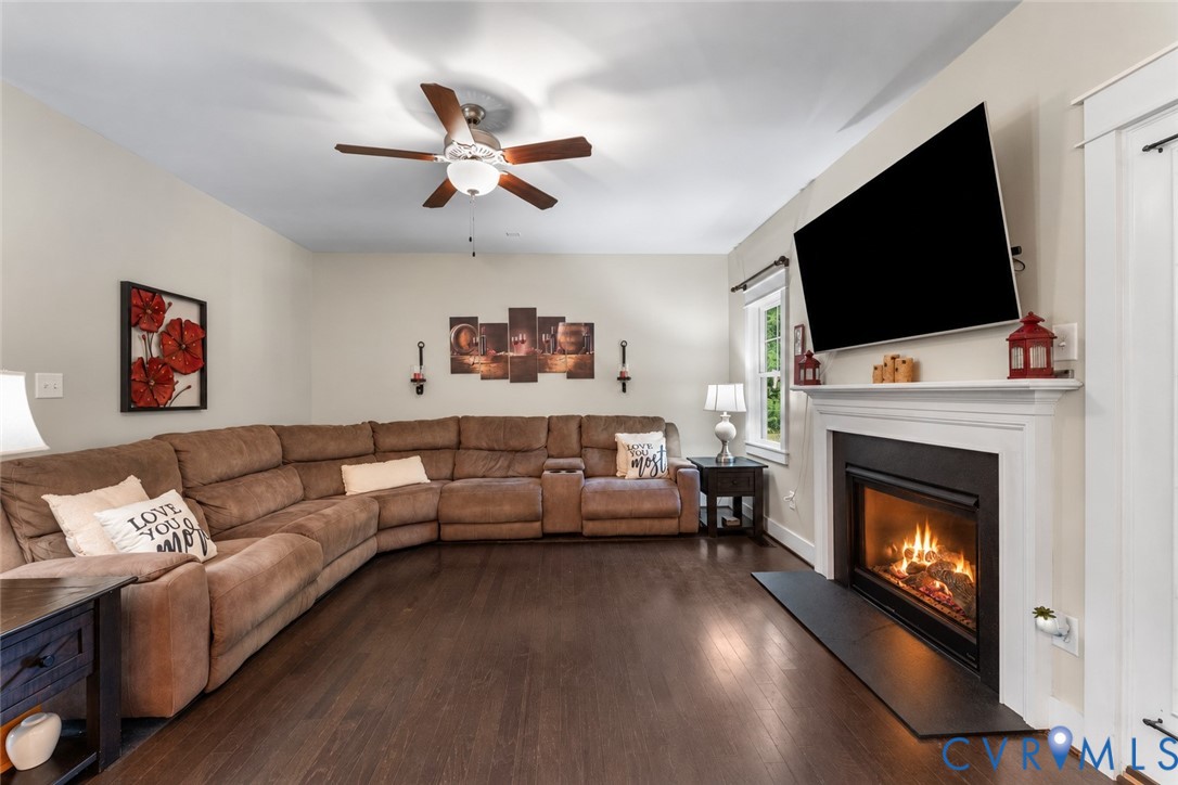 Living space featuring wood-finish flooring, a ceiling fan with integrated lighting, a built-in fireplace, and a white mantel