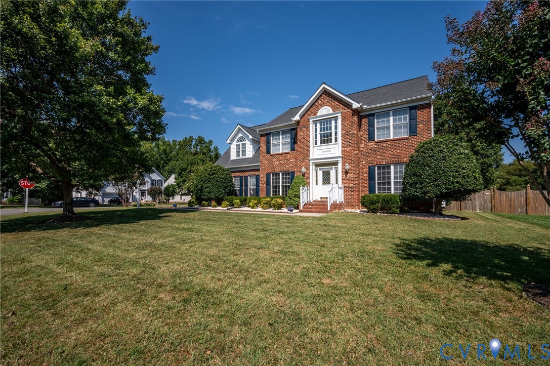 Brick colonial-style residence featuring a prominent front entrance, white columns, and black shutters