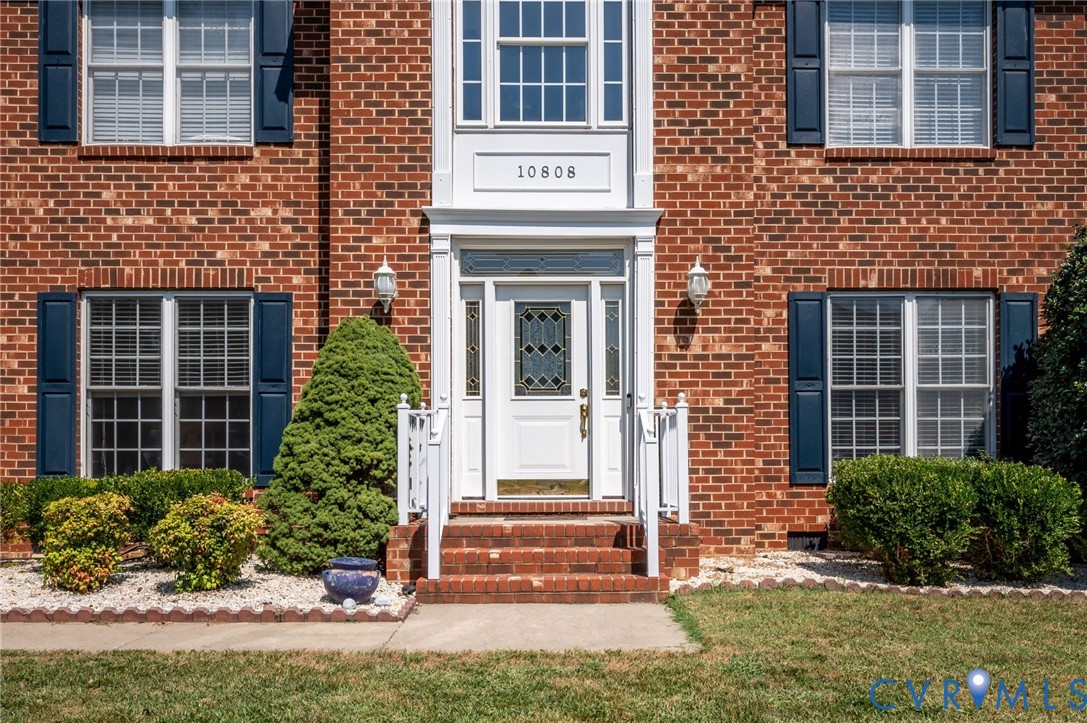 Brick exterior with white trim, a decorative front door with leaded glass, and white porch railings