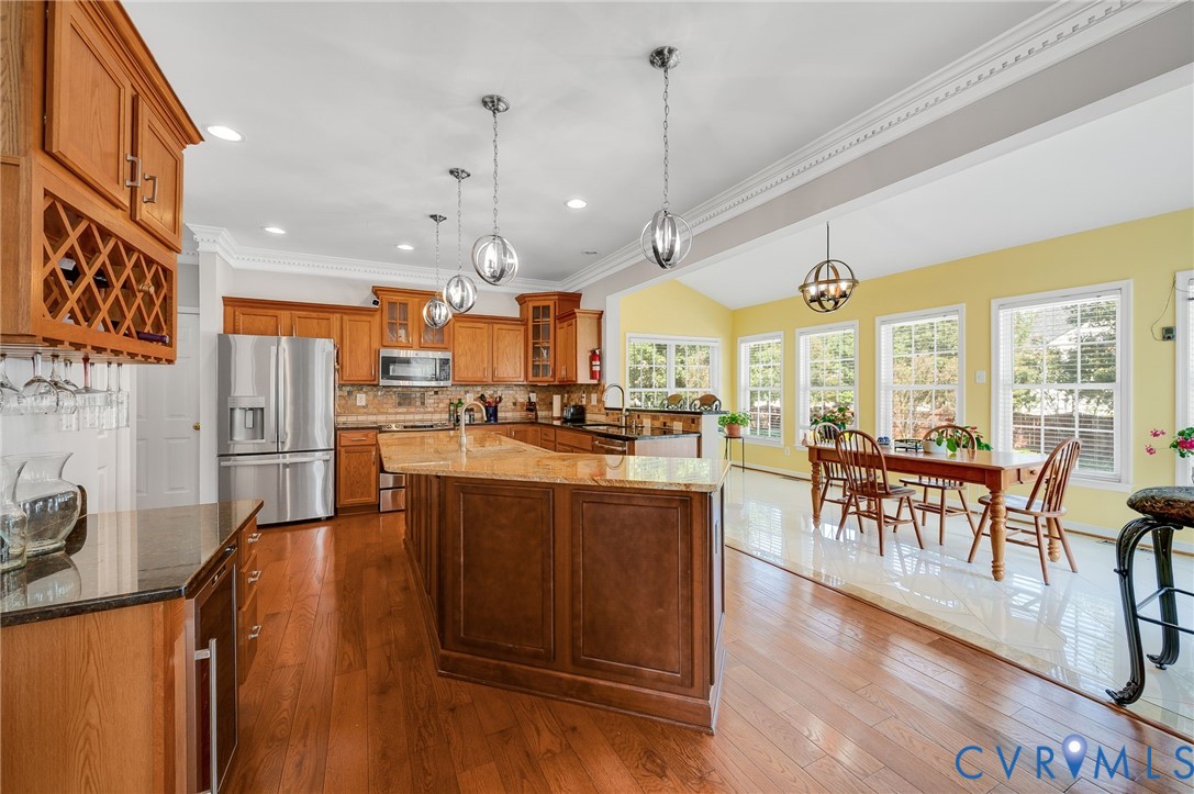 Kitchen featuring wood cabinetry, stainless steel appliances, a center island with a stone-finish countertop, and wood-finish flooring