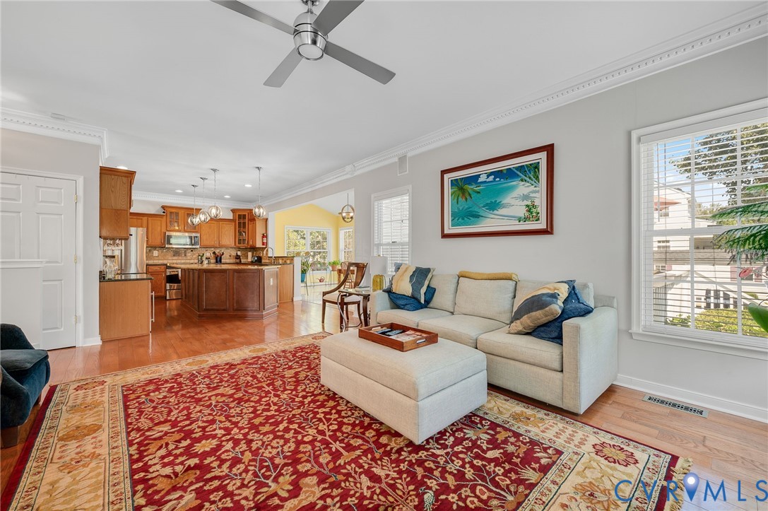 Wood-finish flooring throughout, crown molding detail, recessed lighting, ceiling fan, and large windows with blinds