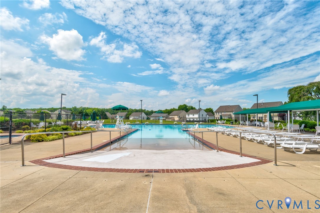Community swimming pool featuring a concrete deck and surrounding lounge area with a green awning