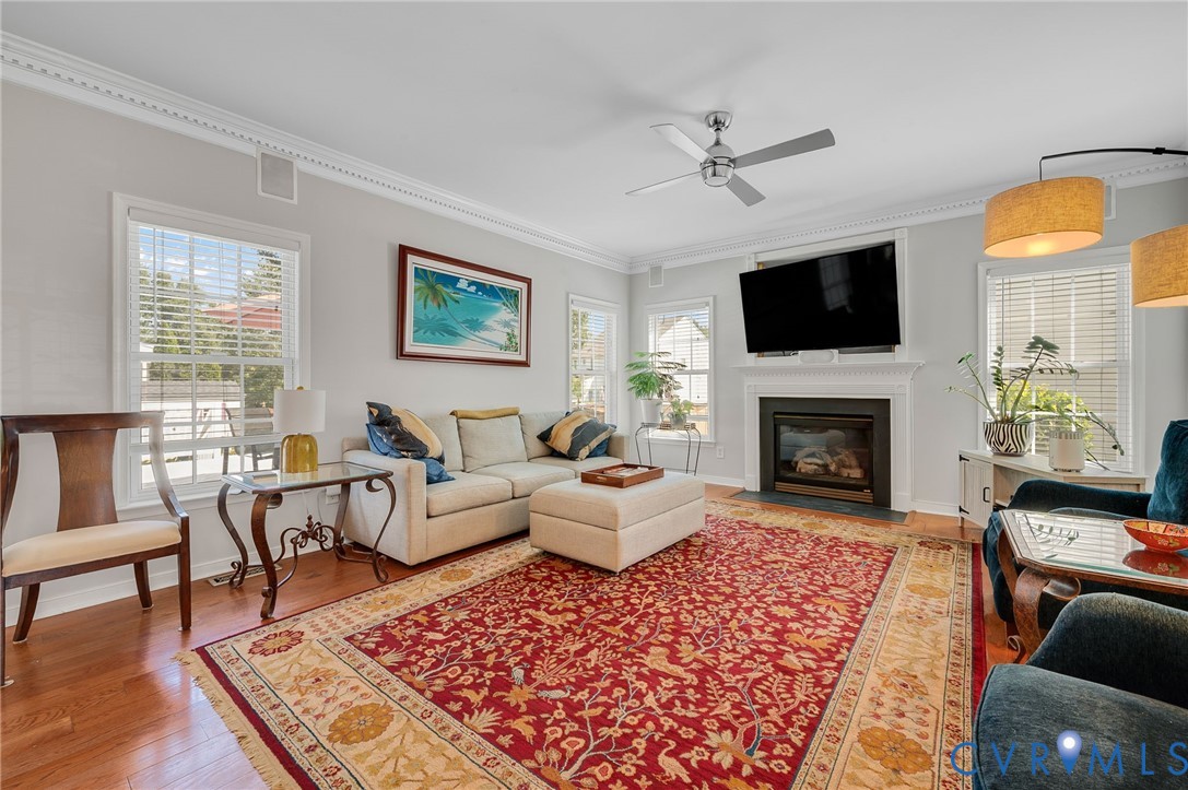 Hardwood flooring, crown molding, a built-in fireplace, multiple windows, and a ceiling fan