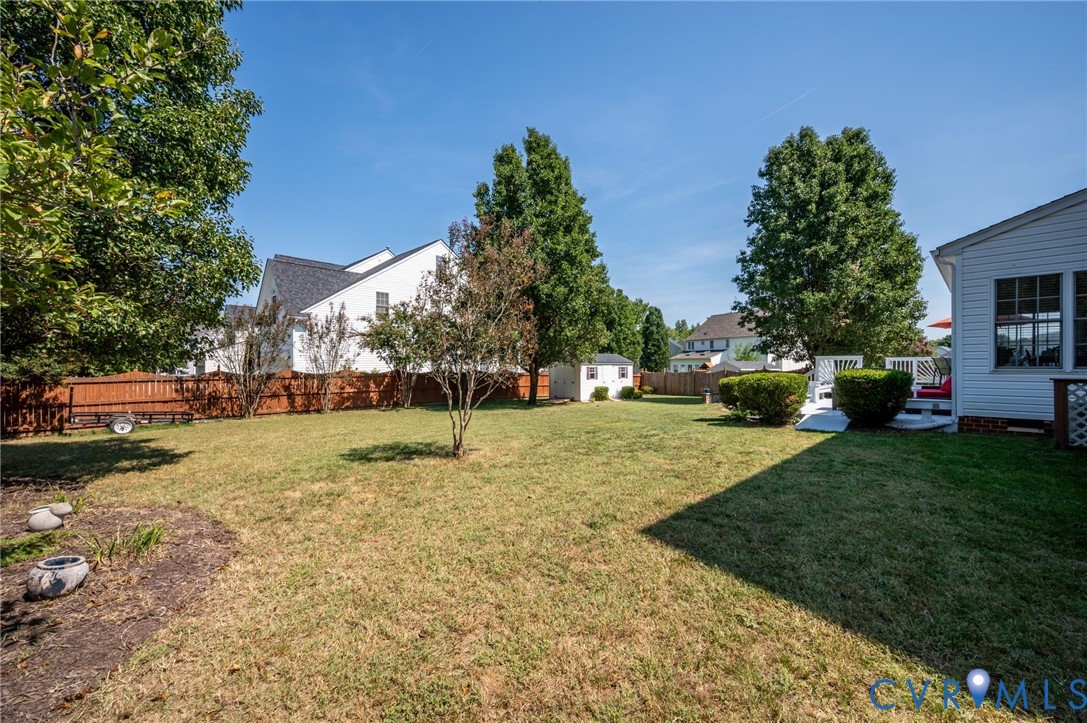 Expansive lawn with mature trees, privacy fencing, a white storage shed, and a composite deck with white railings