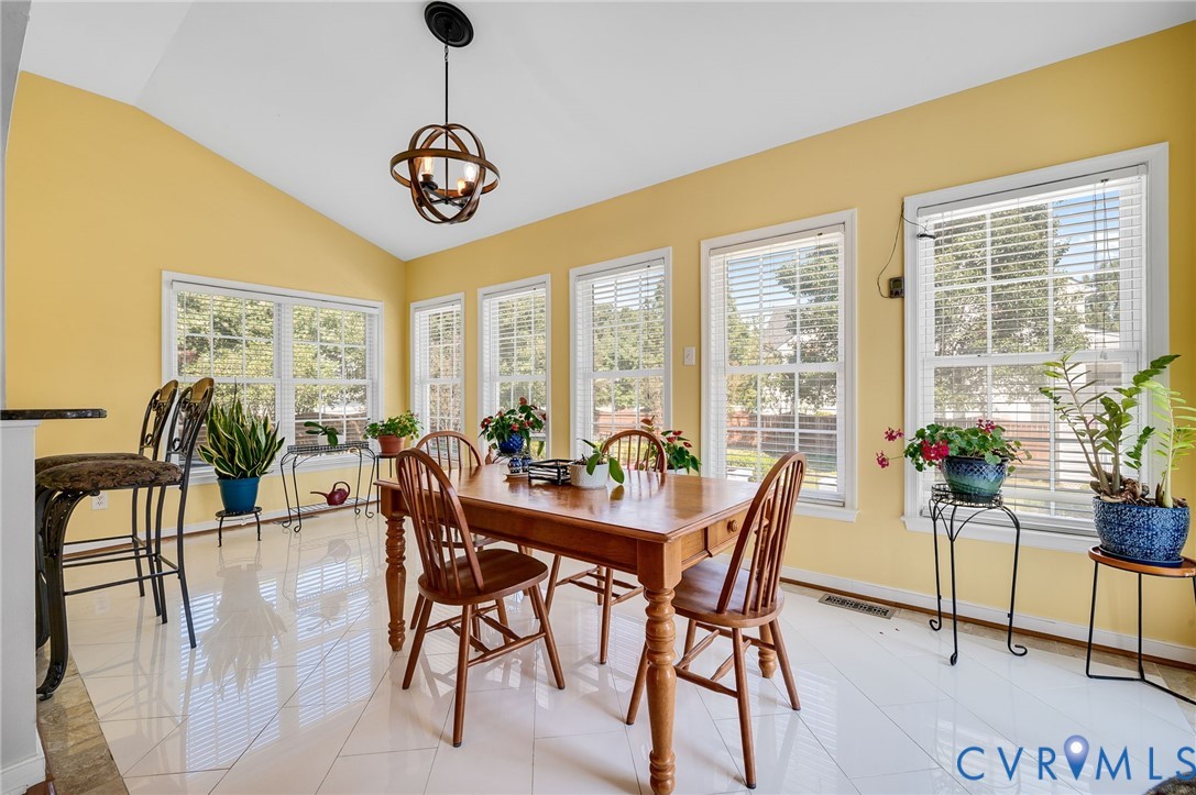 Vaulted ceiling with an orb pendant light fixture, multiple windows, and light-toned tile flooring