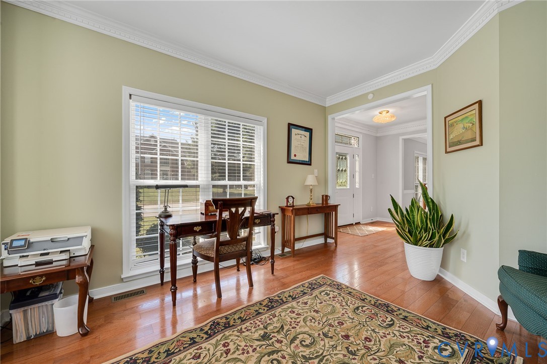 Hardwood flooring, crown molding, large window, and broad arched entryway