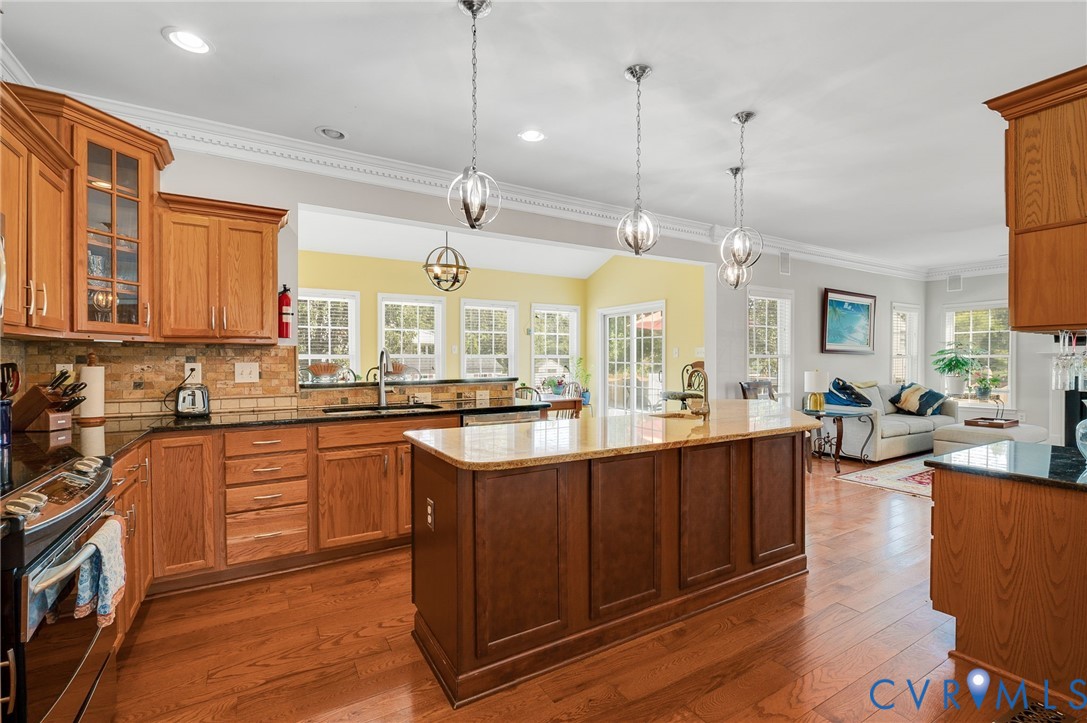 Hardwood flooring throughout, kitchen featuring wood cabinetry and dark countertops, central island with lighter countertop, recessed lighting, and multiple pendant light fixtures