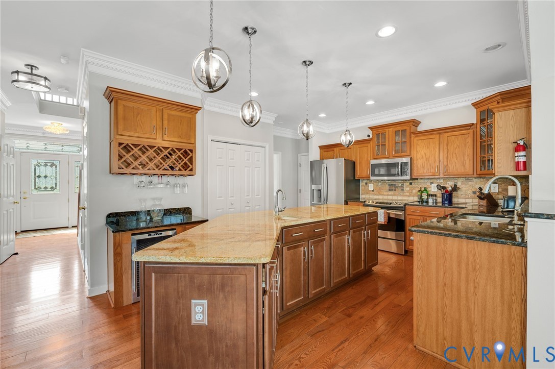 Kitchen featuring wood-finish flooring, an expansive island with a light-toned countertop, stainless steel appliances, and wood cabinetry with a built-in wine rack