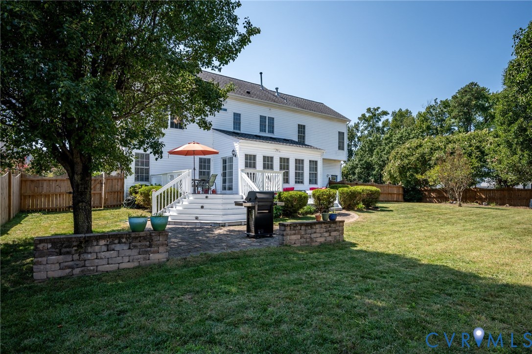 Rear exterior featuring a white multi-story residence, a multi-level white deck, a stone retaining wall, and a wood privacy fence