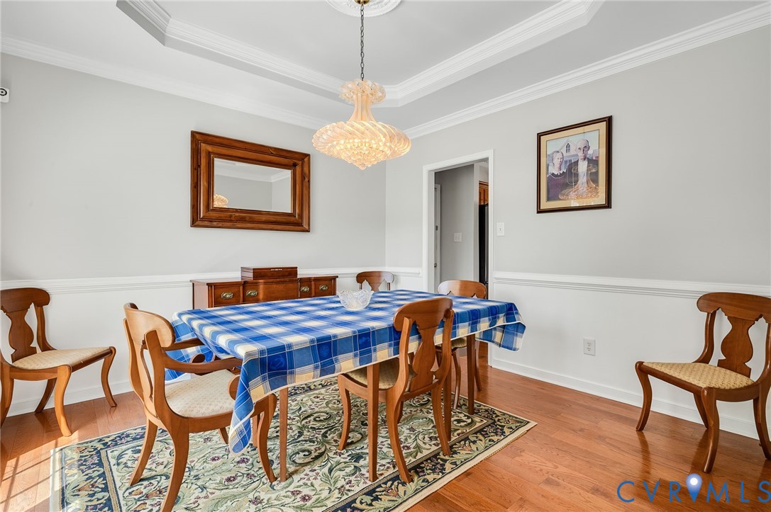 Tray ceiling with crown molding, chandelier, wood-finish flooring, wainscoting, and wall molding