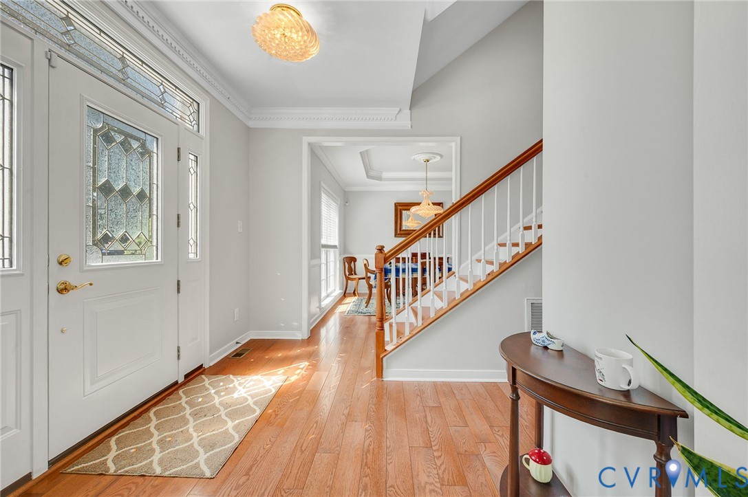 Entryway featuring wood-finish flooring, a white front door with decorative glass, and a staircase with white spindles and a wood handrail
