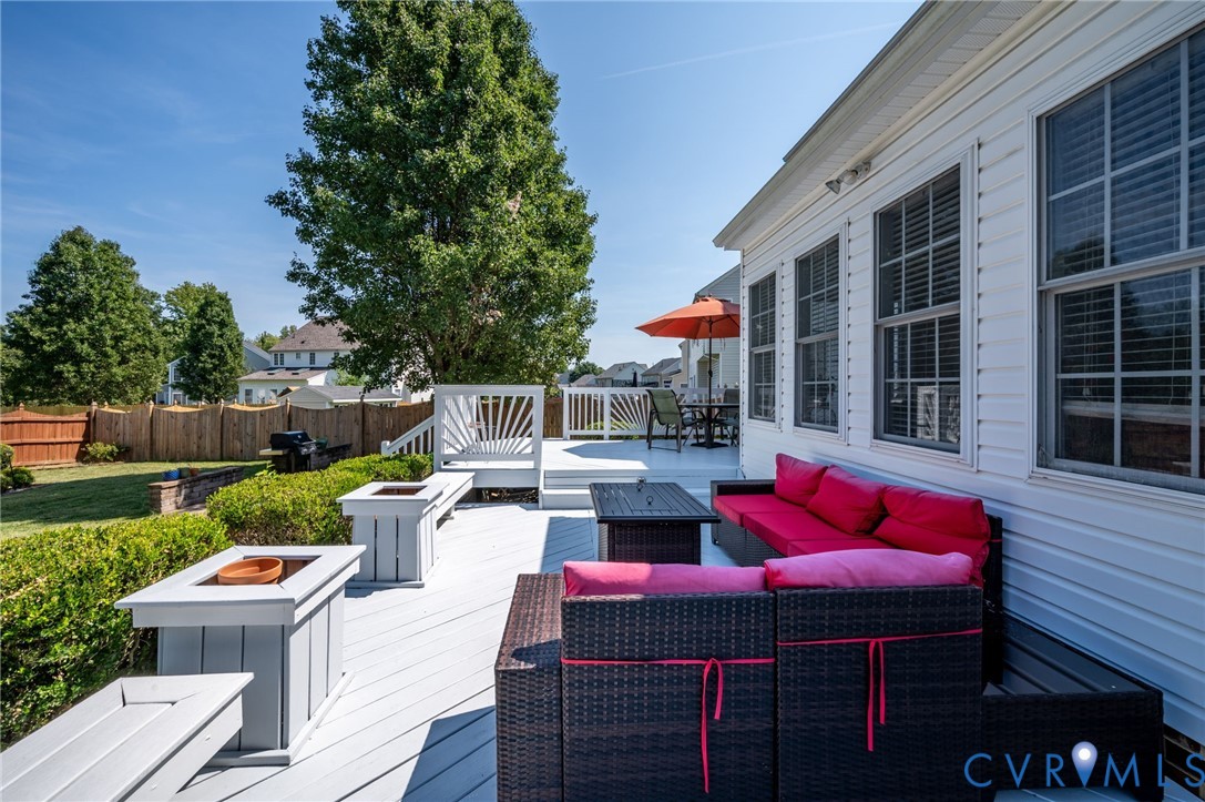 Expansive composite deck featuring multiple entertaining zones with built-in seating, integrated fire pit, and mature landscaping with privacy hedging