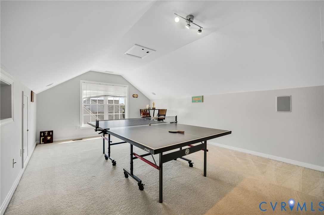 Carpeted room featuring a window with blinds, sloped ceilings, track lighting, and built-in wall speakers