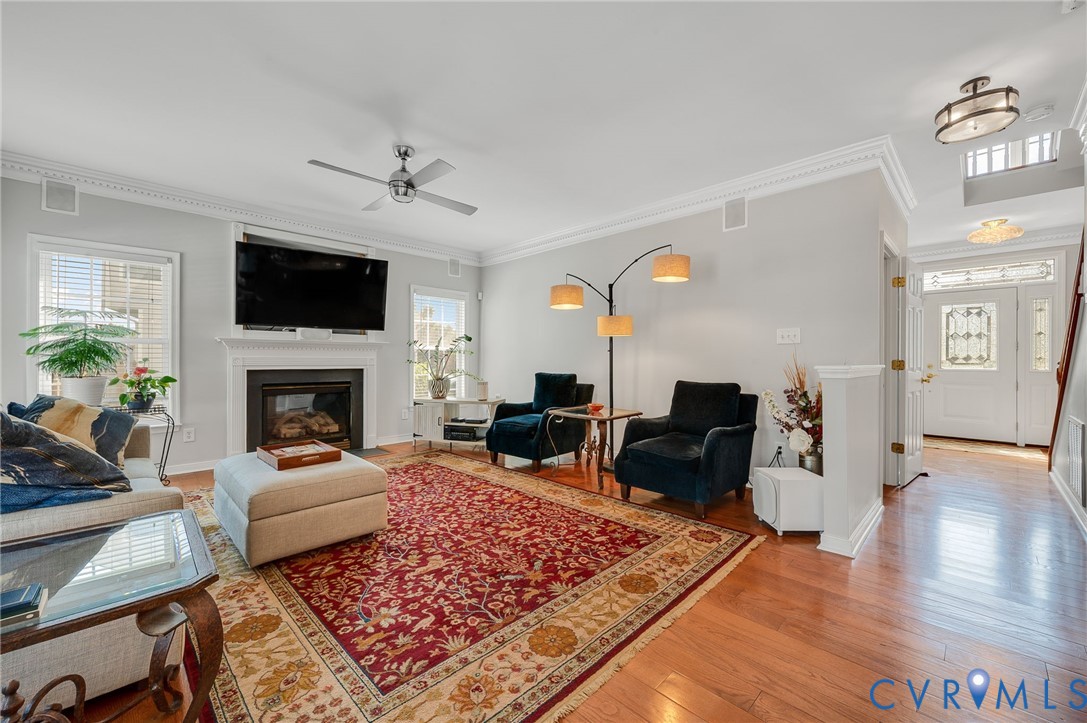 Hardwood flooring throughout, crown molding, built-in fireplace with mantel, ceiling fan, and decorative glass entry door