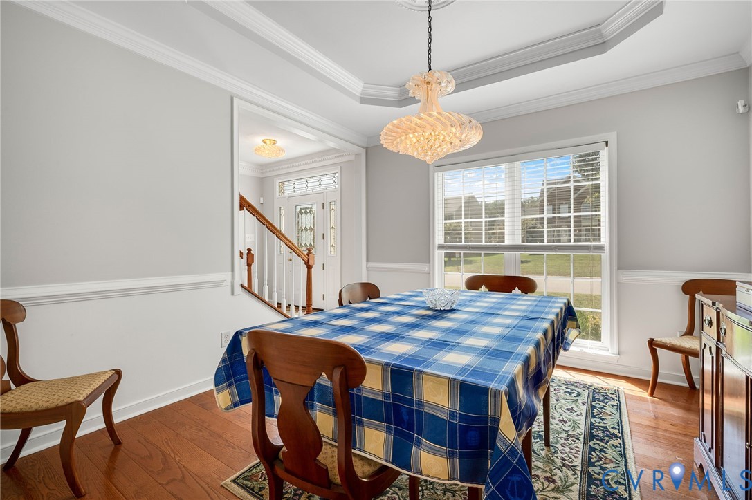 Tray ceiling, crown molding, chair rail, wood-finish flooring, and a decorative chandelier