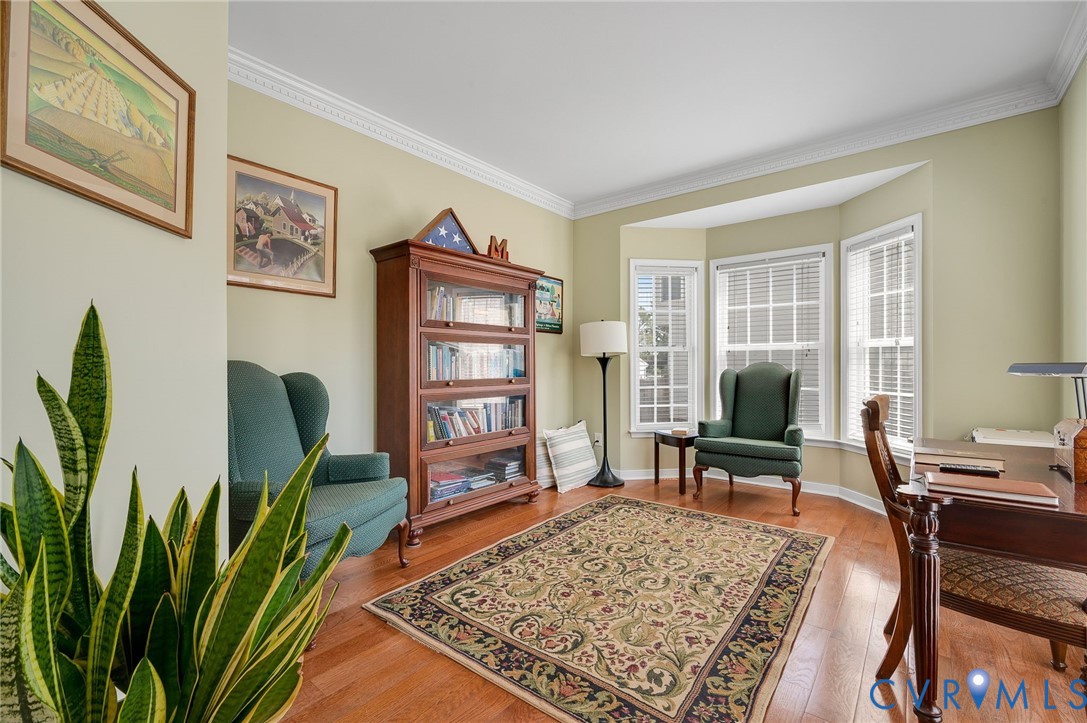Bay window with white blinds, crown molding, wood-finish flooring, and built-in wood cabinetry