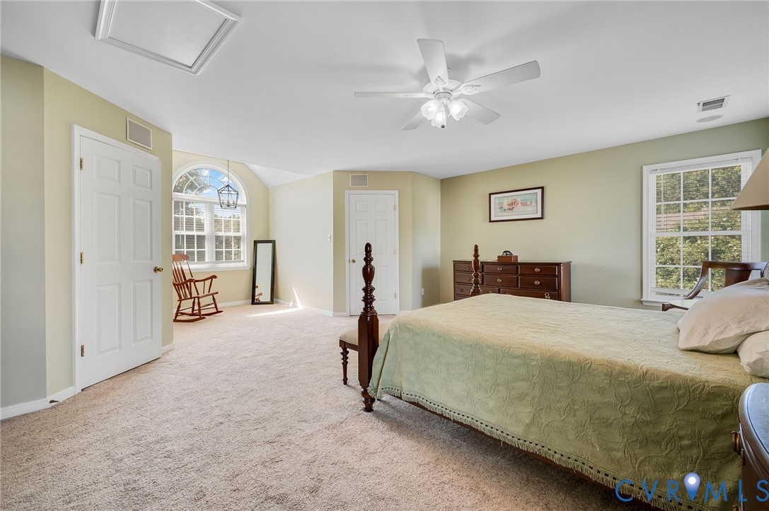 Carpeted flooring, vaulted ceiling, arched window, ceiling fan, and transom window
