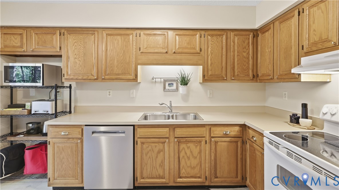 Kitchen featuring wood cabinetry, light-toned countertops, a stainless steel dishwasher, and a double basin sink