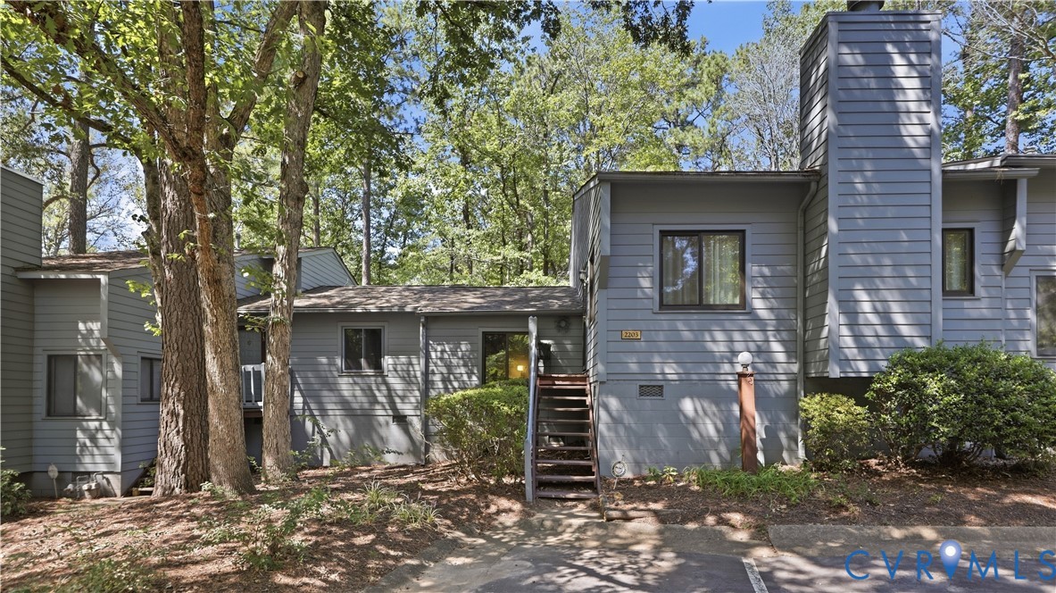 Exterior featuring gray siding, a prominent chimney, dark-trimmed windows, and mature trees Exterior featuring gray siding, a prominent chimney, dark-trimmed windows, and mature trees