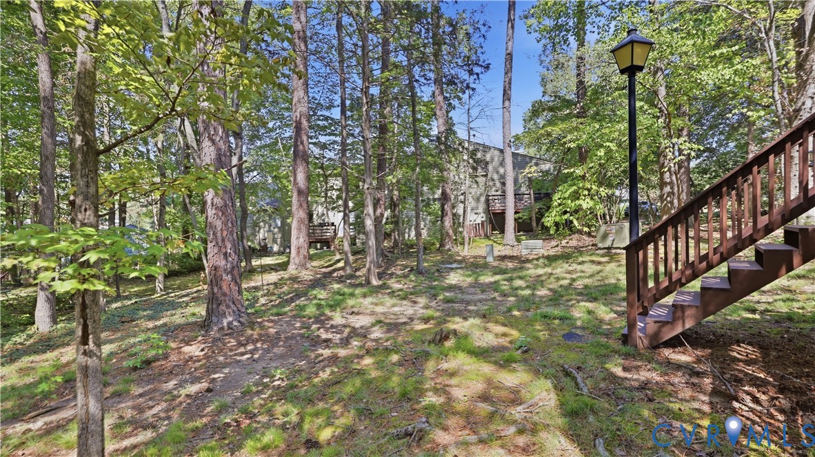 Wooded lot featuring mature trees, a sloped terrain, and a permanent exterior staircase with railing