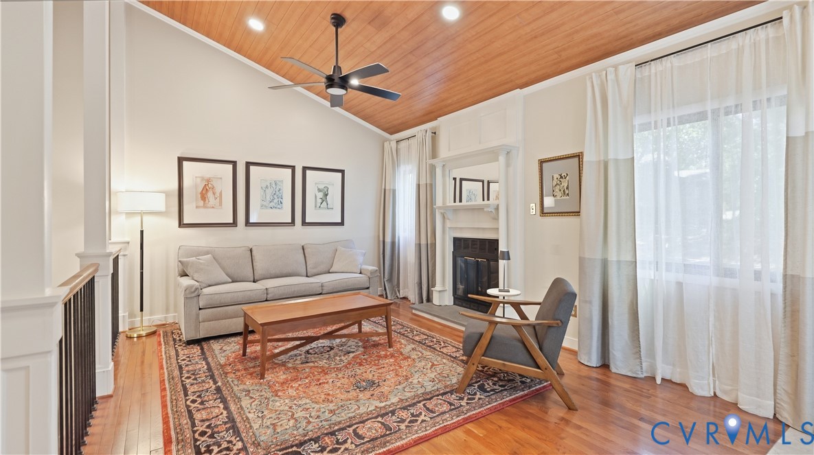 Vaulted wood-paneled ceiling with a ceiling fan, hardwood flooring, and a fireplace with a mantel Vaulted wood-paneled ceiling with a ceiling fan, hardwood flooring, and a fireplace with a mantel
