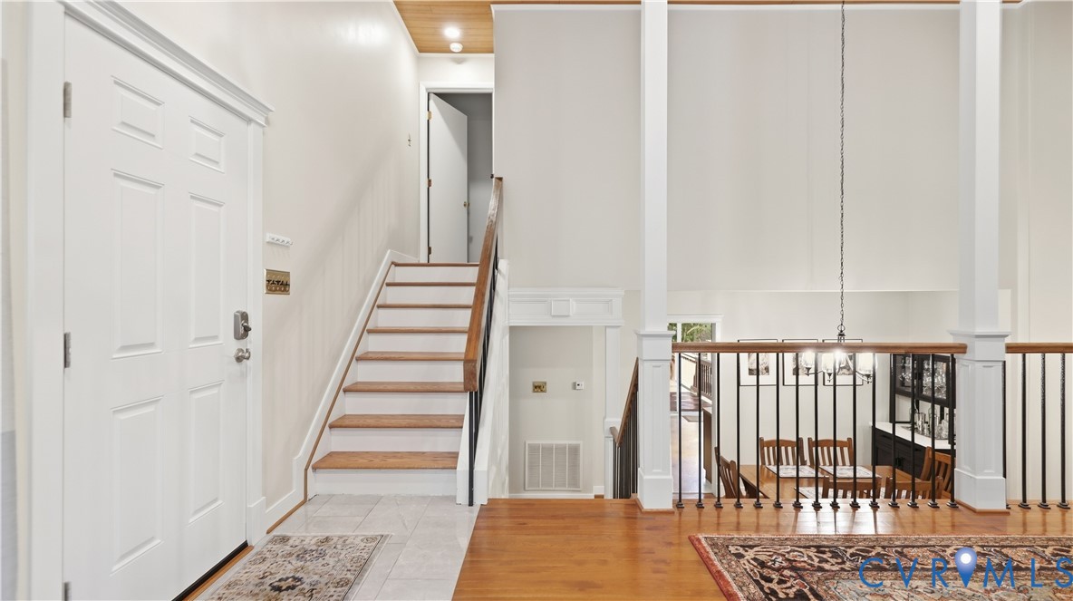 Two-story foyer with hardwood flooring, a white paneled entry door, and a staircase with wood treads and wrought iron balusters