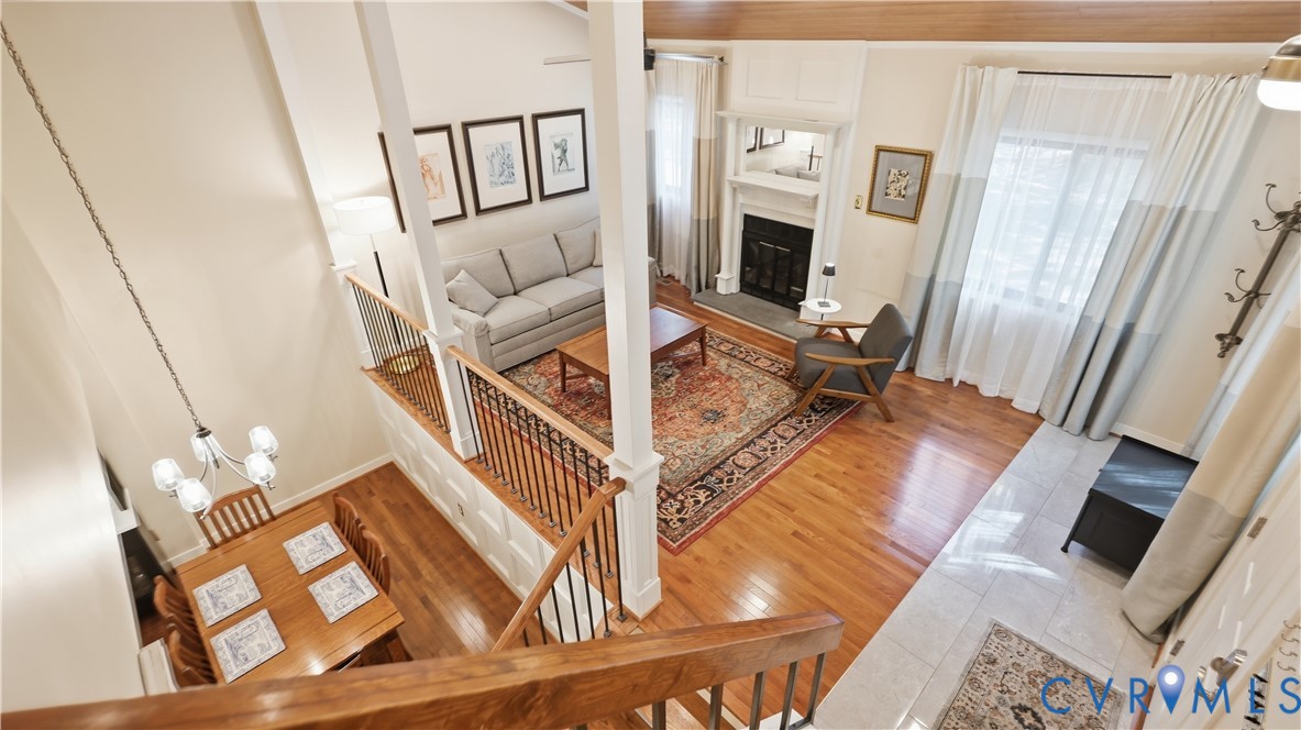 Vaulted ceilings, wood-finish flooring, staircase with wood handrails and wrought iron balusters, fireplace with mantel, and tile flooring
