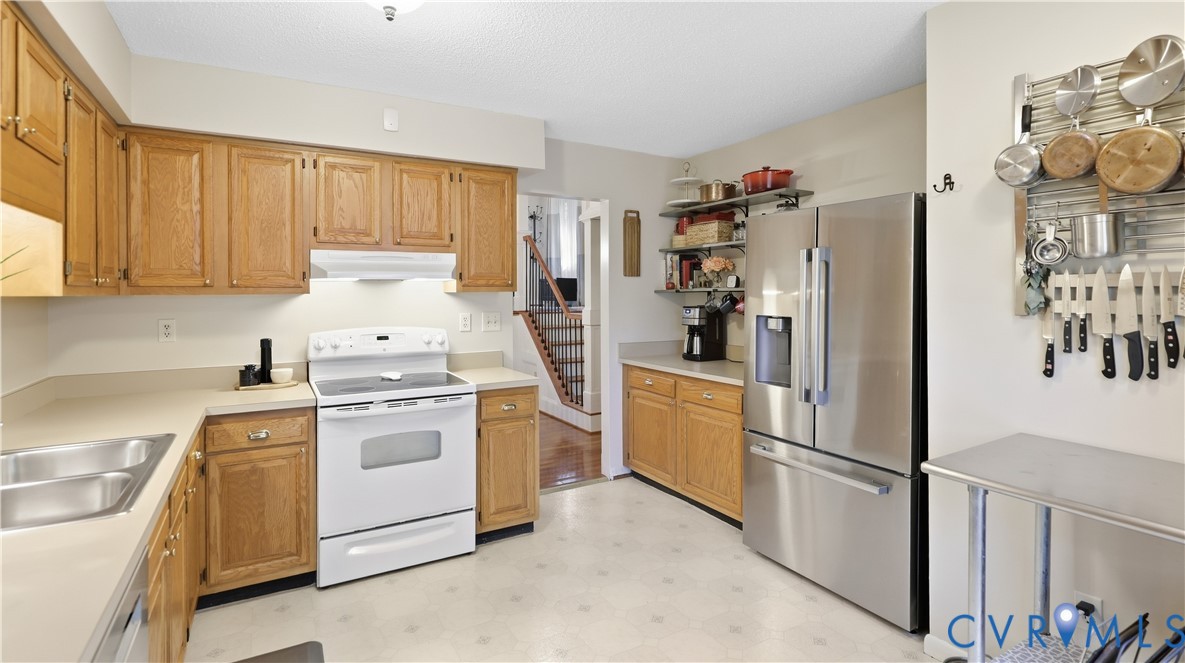 Kitchen featuring wood cabinetry, solid surface countertops, double basin sink, and a stainless steel refrigerator