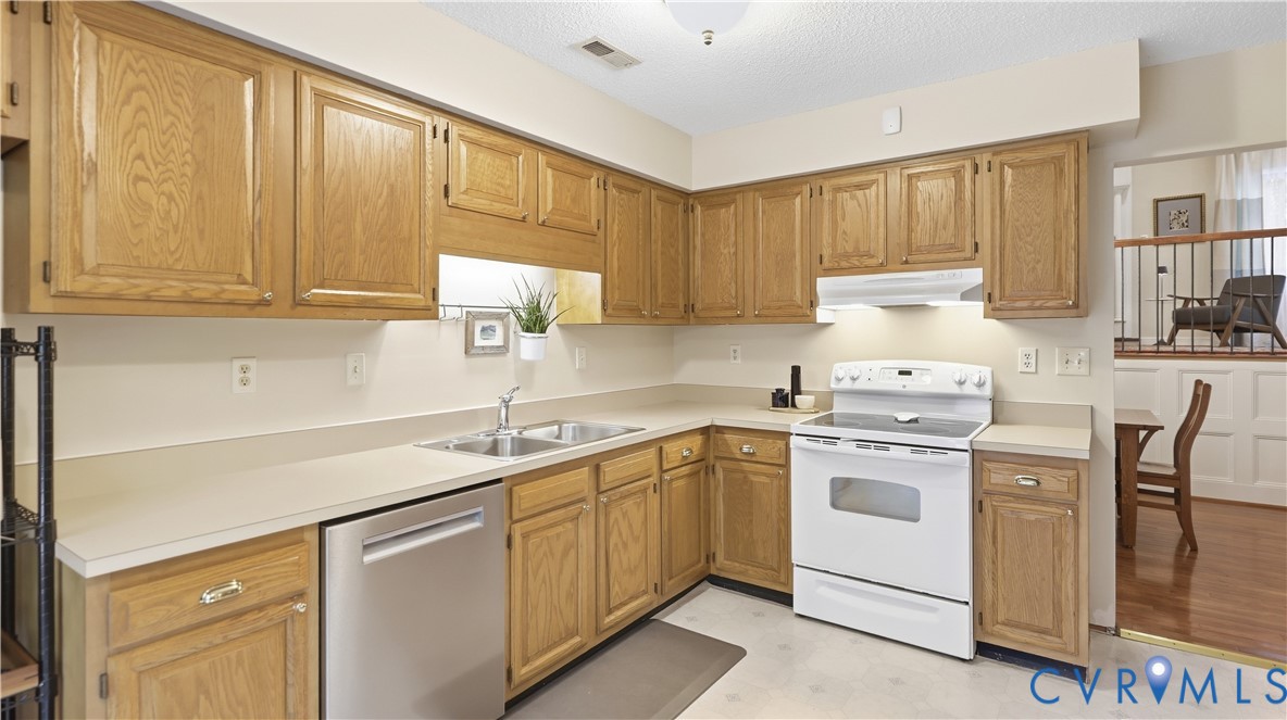 Kitchen featuring wood cabinetry, white countertops, stainless steel dishwasher, and white appliances