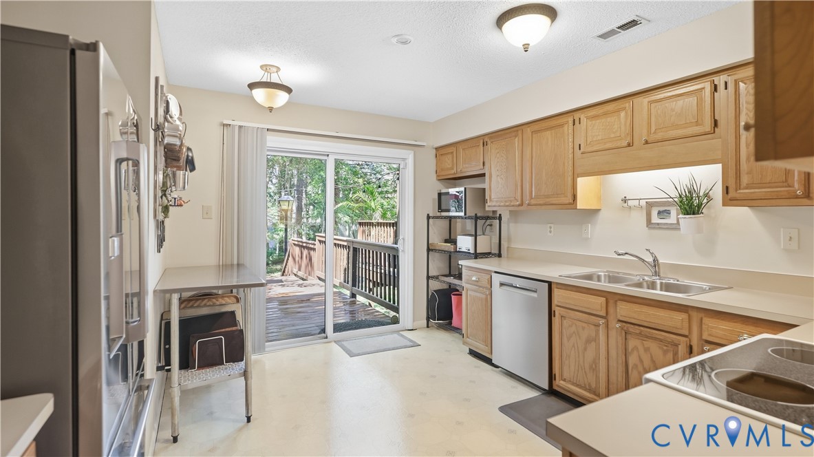 Kitchen featuring wood cabinetry, stainless steel dishwasher, double basin sink, and a sliding glass door leading to an outdoor deck