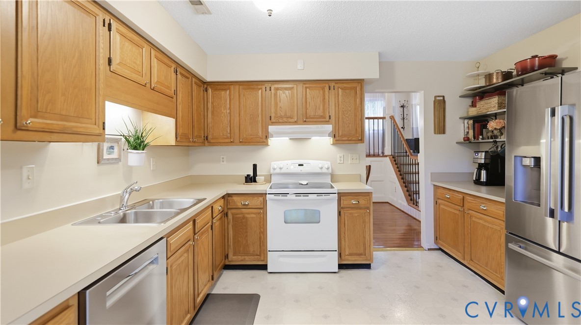Kitchen featuring wood-finish cabinetry, light countertops, stainless steel double basin sink, and stainless steel dishwasher