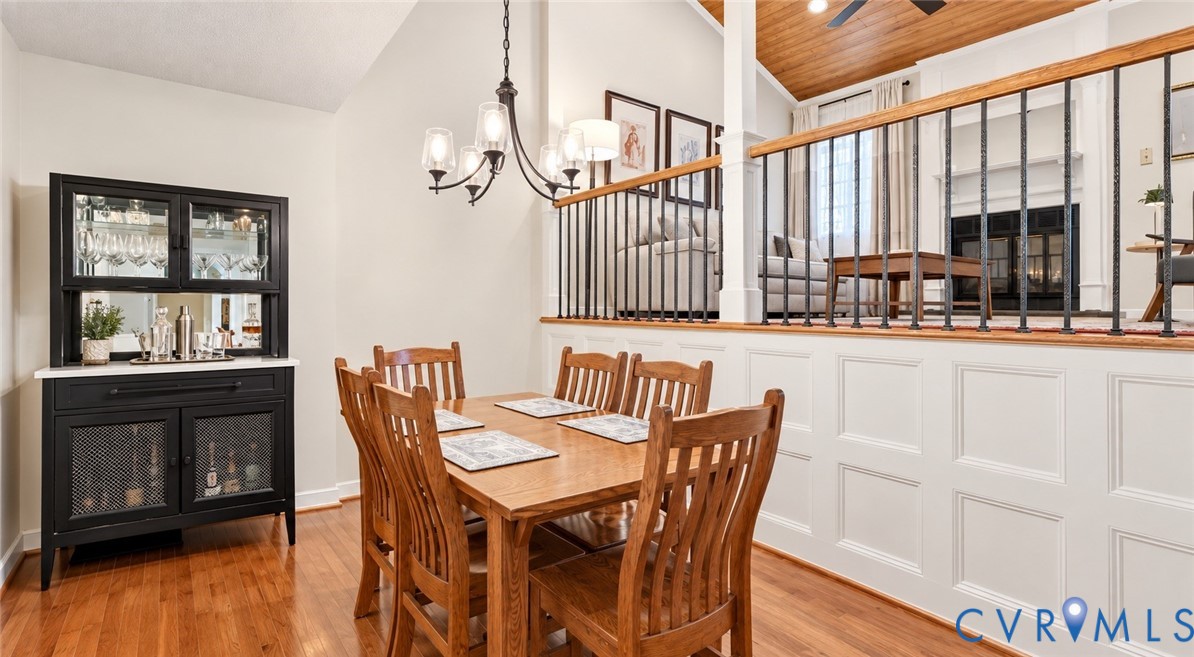 Hardwood flooring, vaulted ceiling, traditional chandelier, wainscoting, and wrought iron balusters