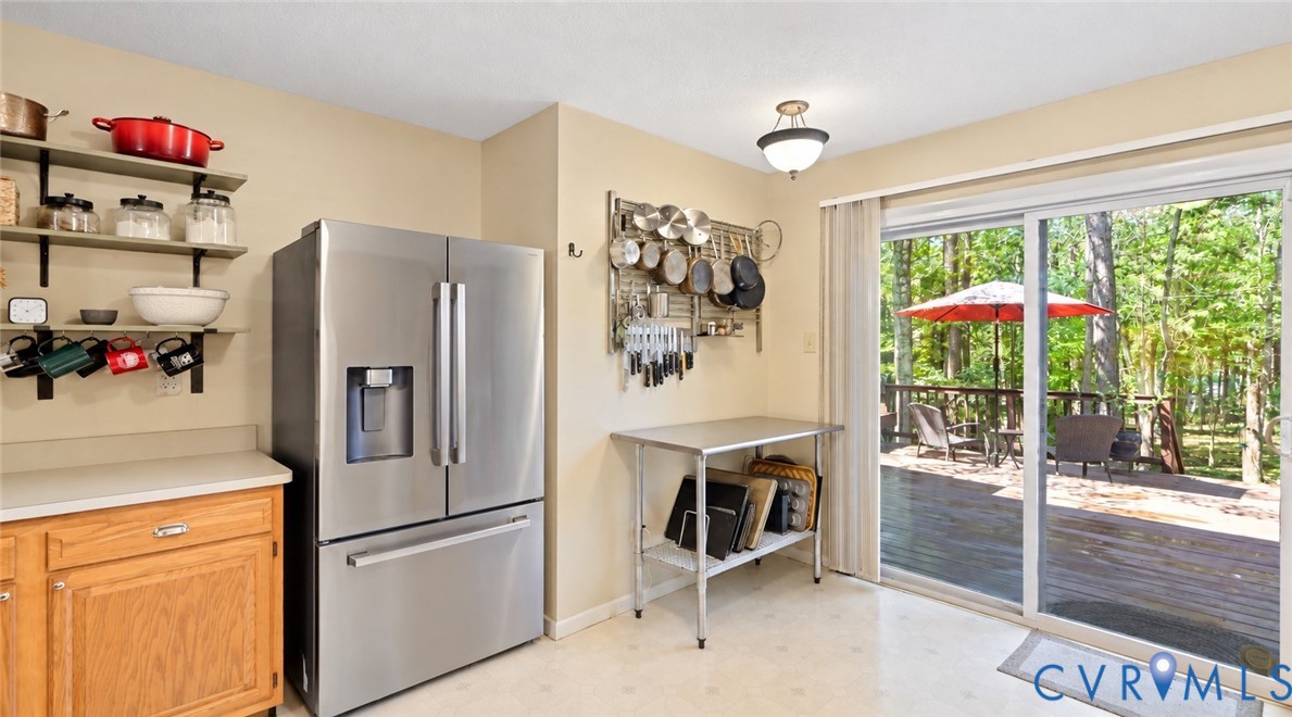 Stainless steel French door refrigerator, wood cabinetry, open shelving, and sliding glass doors leading to an outdoor deck