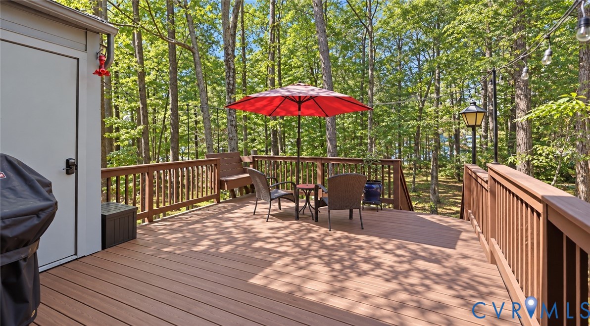Expansive wood-finish deck with integrated railing, surrounded by mature trees, featuring a built-in outdoor lighting fixture