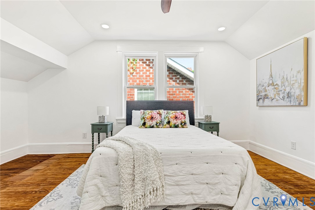 Hardwood flooring, recessed ceiling lighting, window with brick exterior, angled ceilings, and a ceiling fan