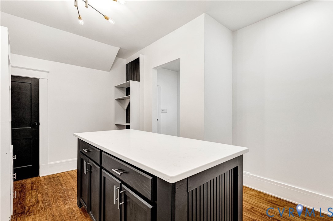 Central island with a white countertop and dark cabinetry, wood-finish flooring, built-in shelving, and a modern ceiling fixture