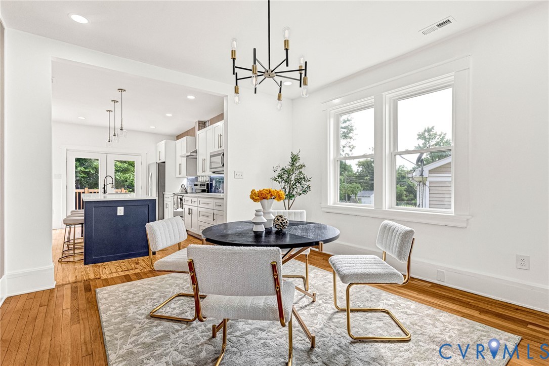 Hardwood flooring, crisp white walls, and an open archway leading to a kitchen with white cabinetry and a dark blue island