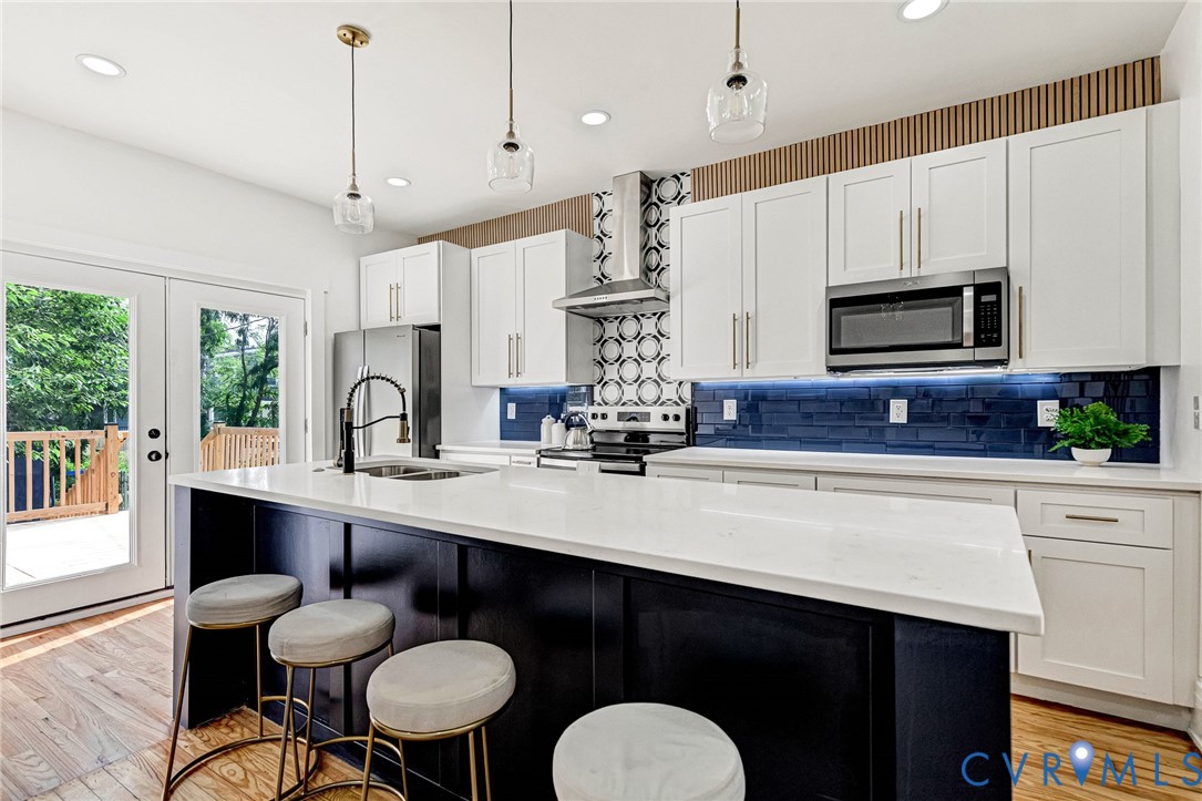 Gourmet kitchen featuring a large central island with white countertop, stainless steel appliances, white cabinetry, and a blue tile backsplash