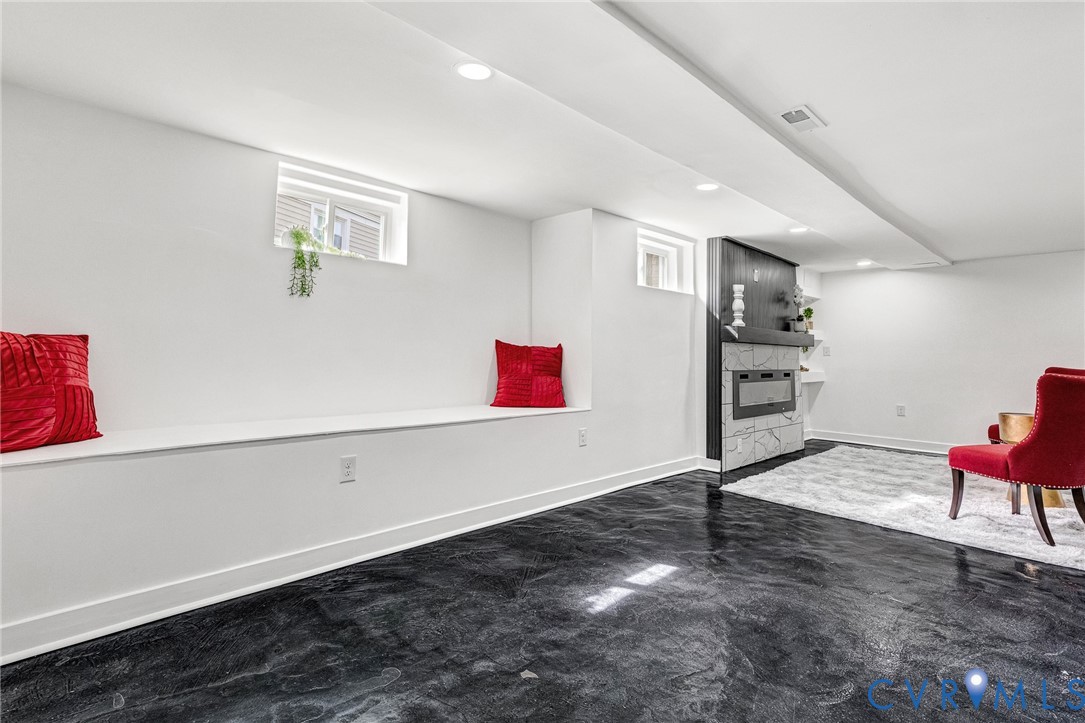 Recessed lighting illuminates the modern electric fireplace featuring a light-toned stone surround