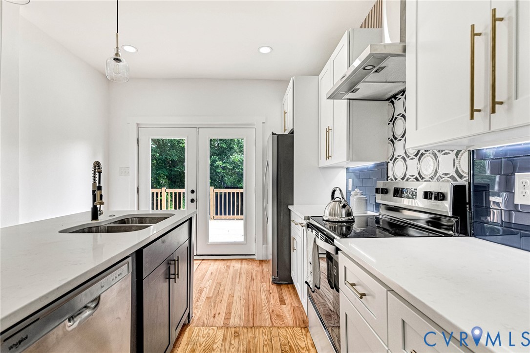 Contemporary kitchen featuring white cabinetry, light-toned countertops, hardwood flooring, and a decorative tile backsplash