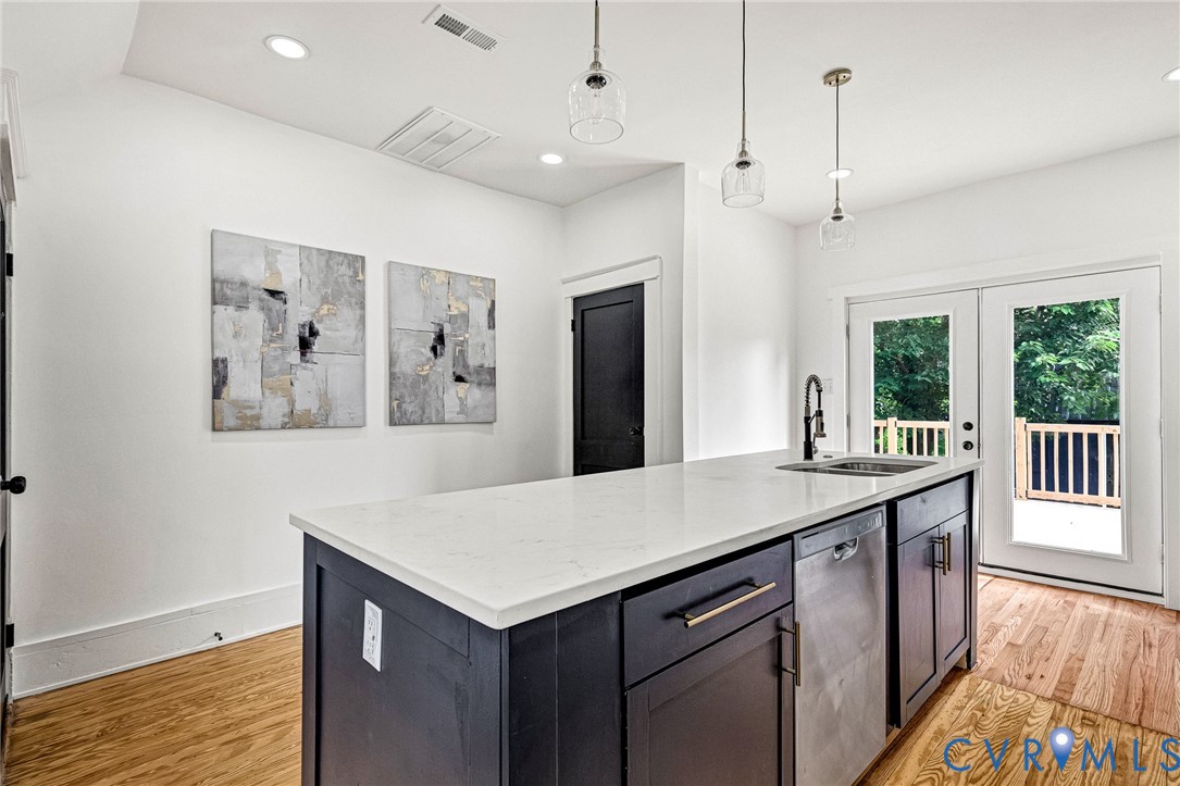Kitchen island with a white countertop and integrated sink, stainless steel dishwasher, wood-finish flooring, recessed lighting, and double glass-paneled doors leading to an outdoor deck