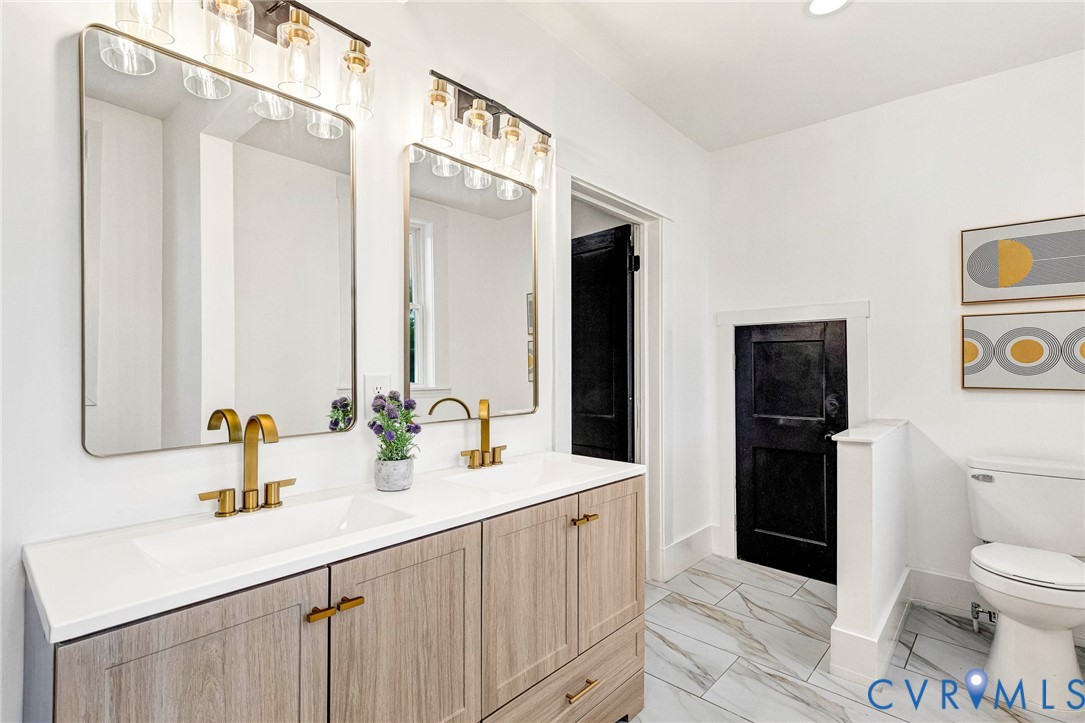 Double vanity with wood-finish cabinetry, white countertop, and gold-tone fixtures