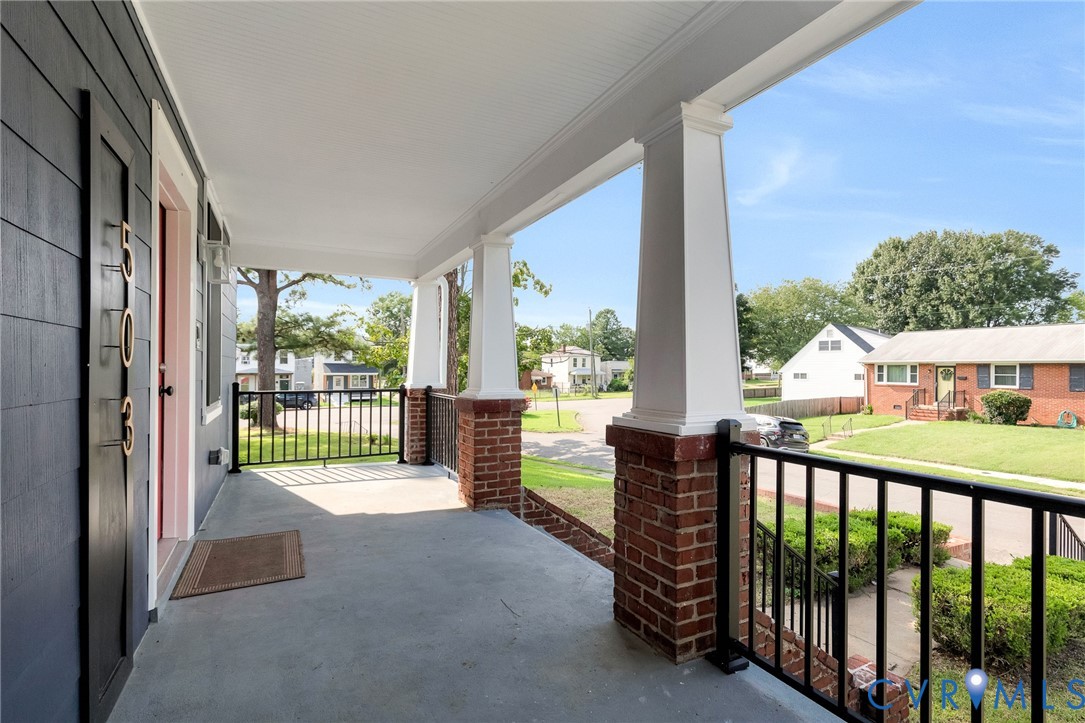 Covered front porch featuring concrete flooring, brick pillars with white columns, and black metal railings